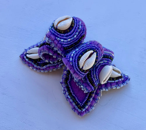 Purple beaded hair clips with shell accents on a light blue background